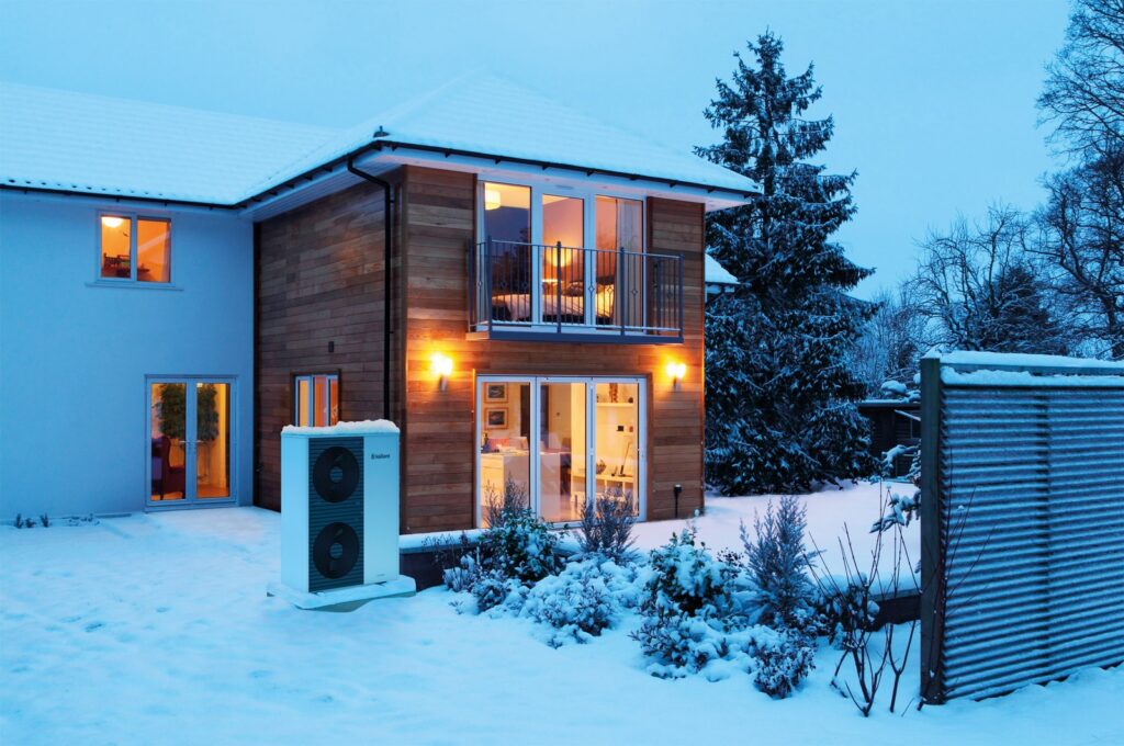 Luft-Wasser-Wärmepumpe vor einem Wohnhaus im Winter.