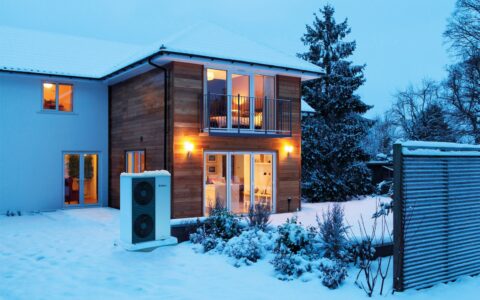 Luft-Wasser-Wärmepumpe vor einem Wohnhaus im Winter.