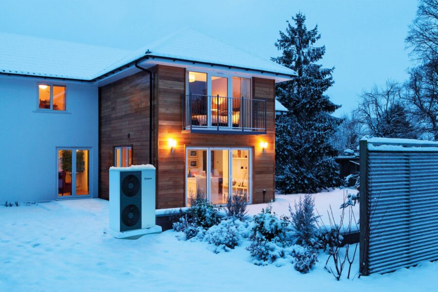 Luft-Wasser-Wärmepumpe vor einem Wohnhaus im Winter.