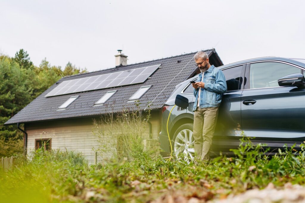 Mann lädt ein Elektroauto vor einem Haus mit Photovoltaikanlage