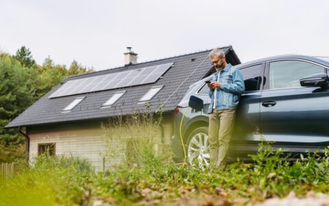 Mann lädt ein Elektroauto vor einem Haus mit Photovoltaikanlage