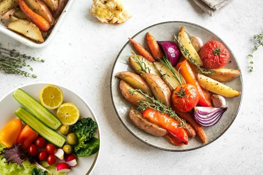 Ofengemüse mit Kartoffeln, Möhren, Tomaten, roten Zwiebeln und Kräutern neben einem frischen Salat.